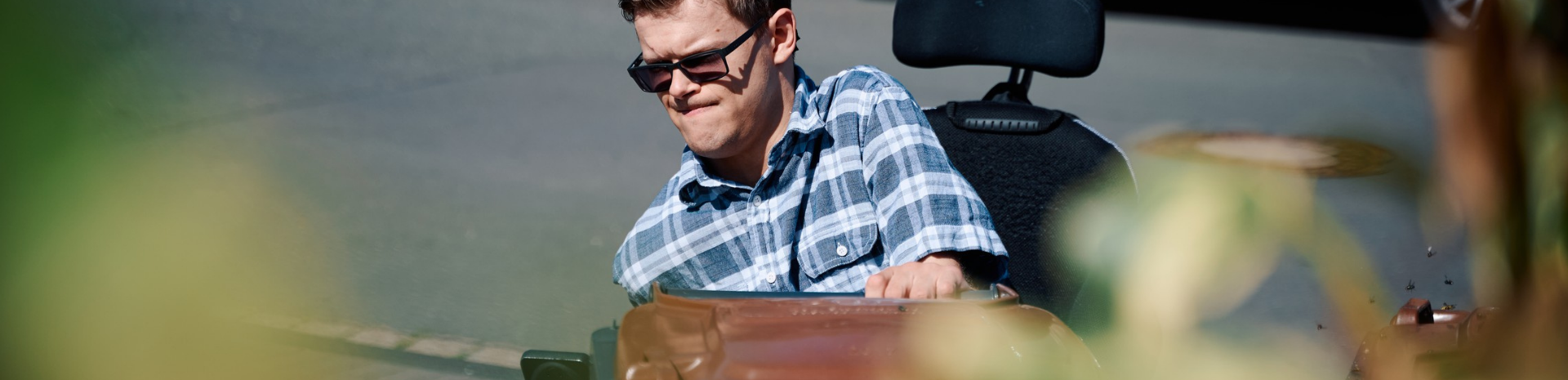 Ein junger Mann mit Sonnenbrille im Rollstuhl zieht eine Bio-Mülltonne